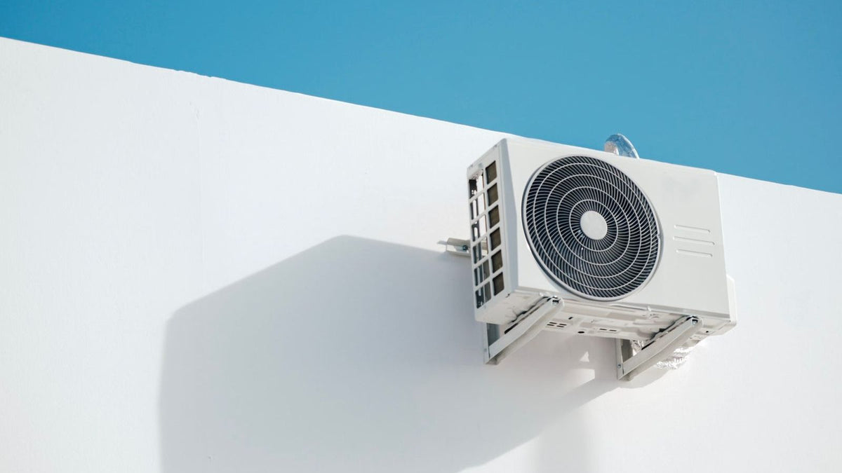 White outdoor AC condenser unit mounted on a wall, illustrating rheem vs goodman 2026 HVAC equipment options
