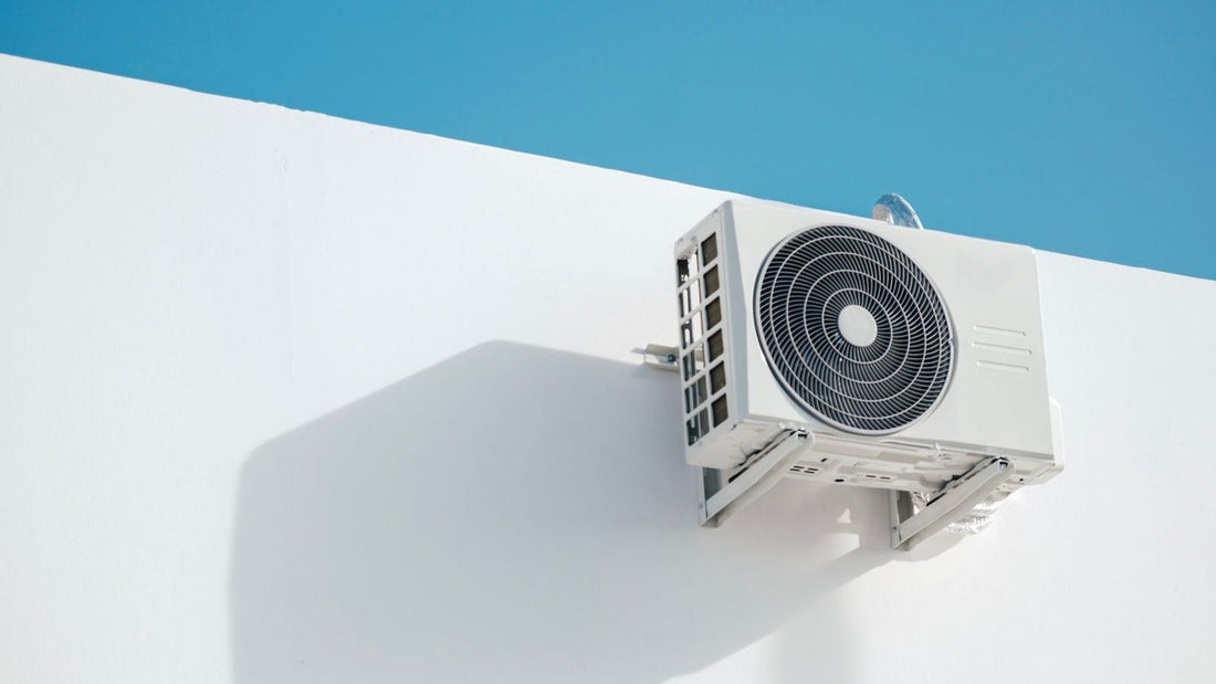 White outdoor heat pump unit mounted on wall with visible fan and ventilation grilles during defrost cycle heat pump operation