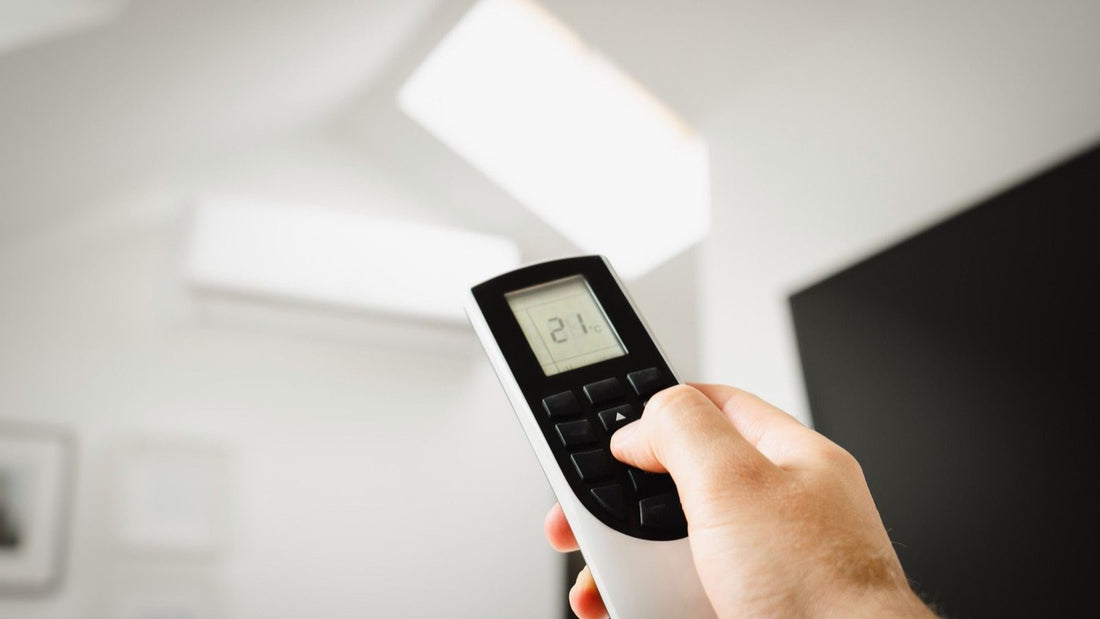 Hand holding remote showing 21°C pointed at ceiling unit with emergency heat on heat pump mode displayed