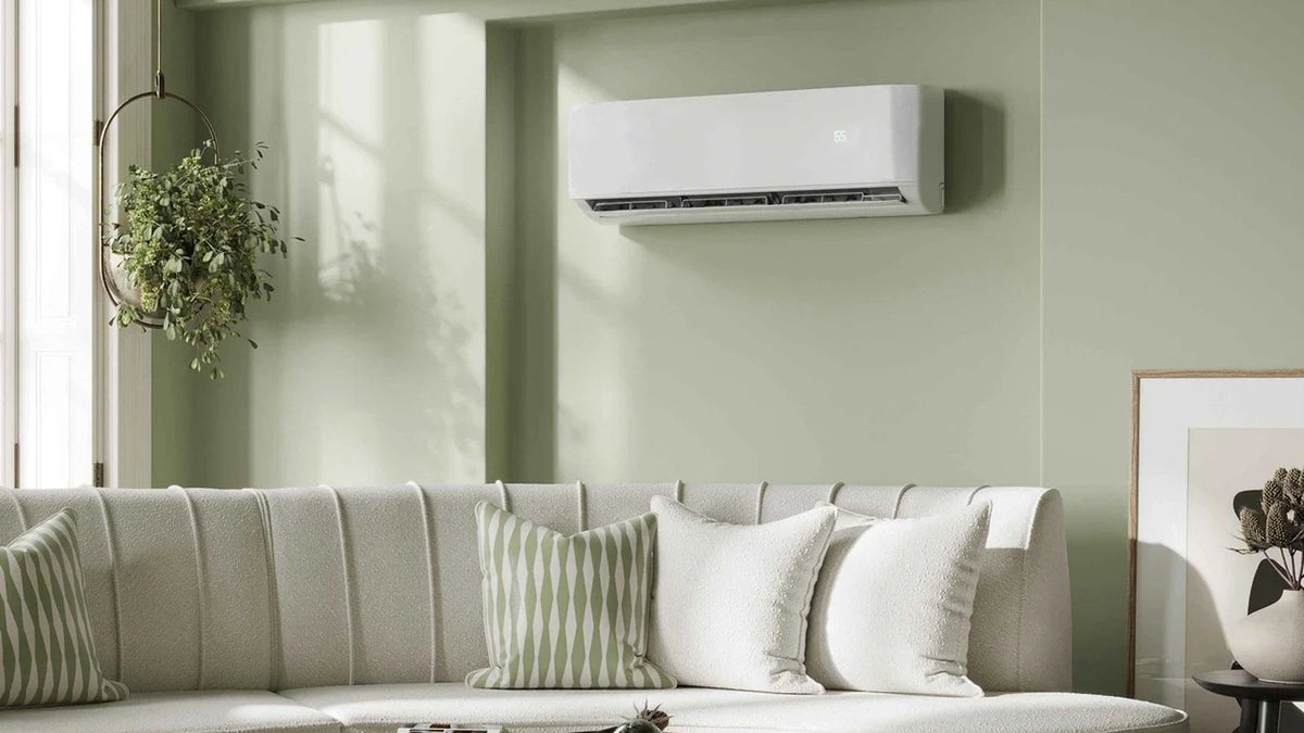 White wall-mount mini split indoor unit above a sofa in a sage green living room, one head of a DIY dual zone mini split system